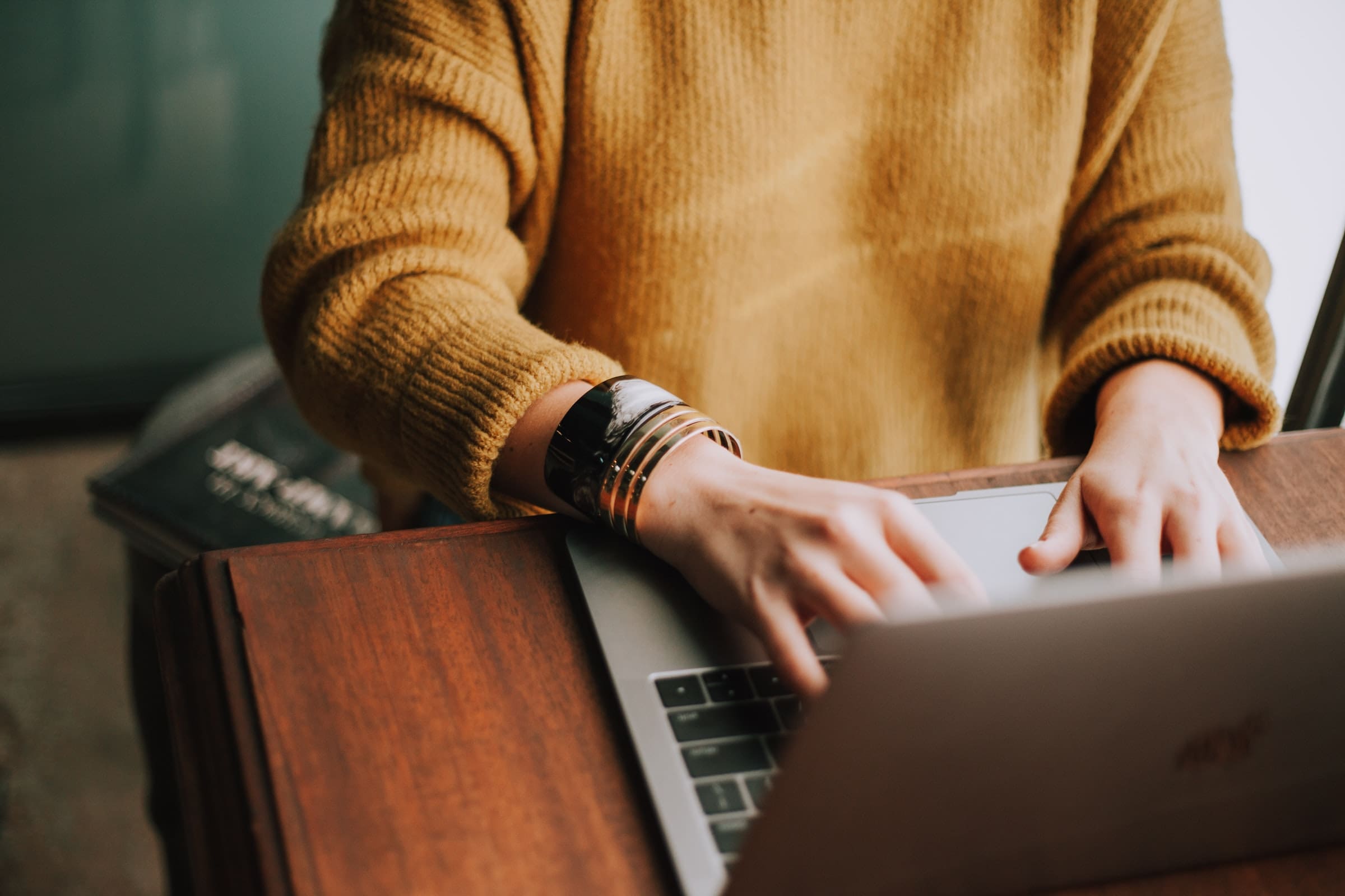 A person in a yellow sweater typing at a computer