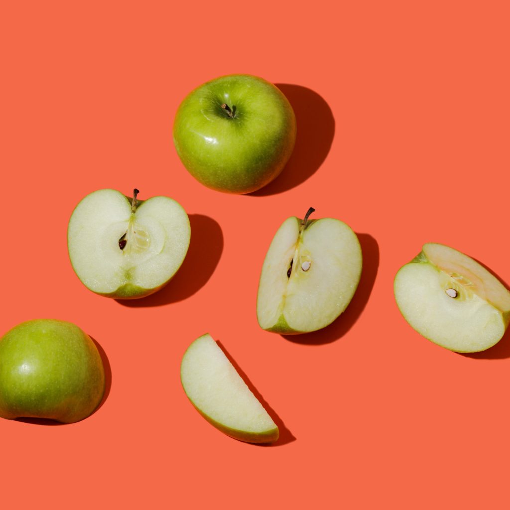 Cut up granny smith apples against an orange backdrop