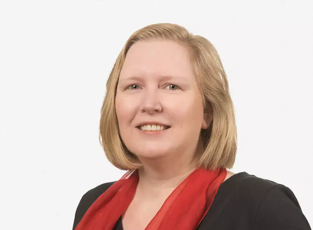 person with short blond hair in a black shirt and red scarf standing in front of white background