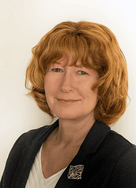 person with red hair and a dark blazer in front of a white background