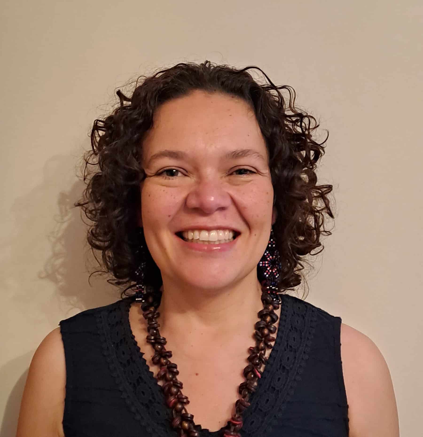 woman smiling with short curly hair, blue shirt and necklace
