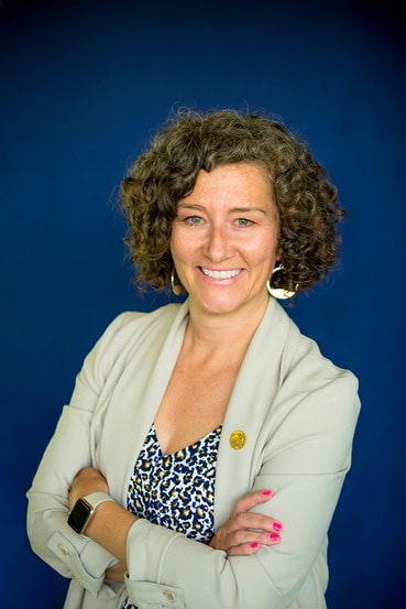 woman with curly hair wearing a cardigan in front of a royal blue background