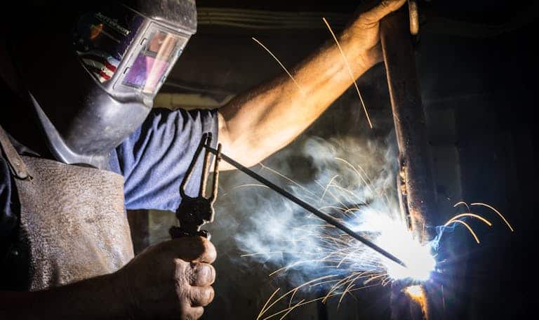 Close-up of a welder in action, showcasing bright sparks and metalworking skill indoors.