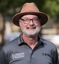 person with a grey beard wearing a brown hat and grey polo shirt