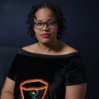 person with dark curly hair, glasses and red lipstick