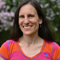 smiling person with dark brown hair and bright pink and orange shirt