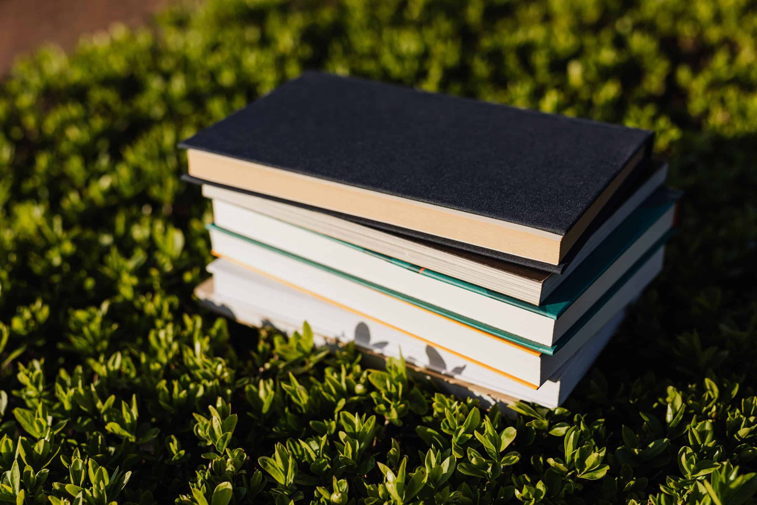 Stack of different books on short bright green park grass in soft evening light at sundown