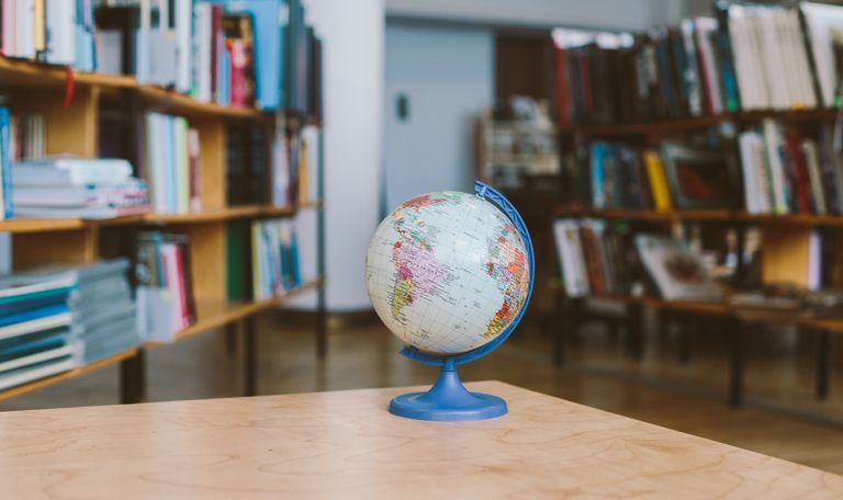A globe in a quiet library setting, surrounded by shelves filled with books, represents education and exploration.